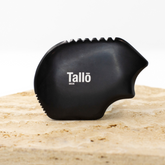 Black skin exfoliator with 'Tallo' branding on a beige surface
