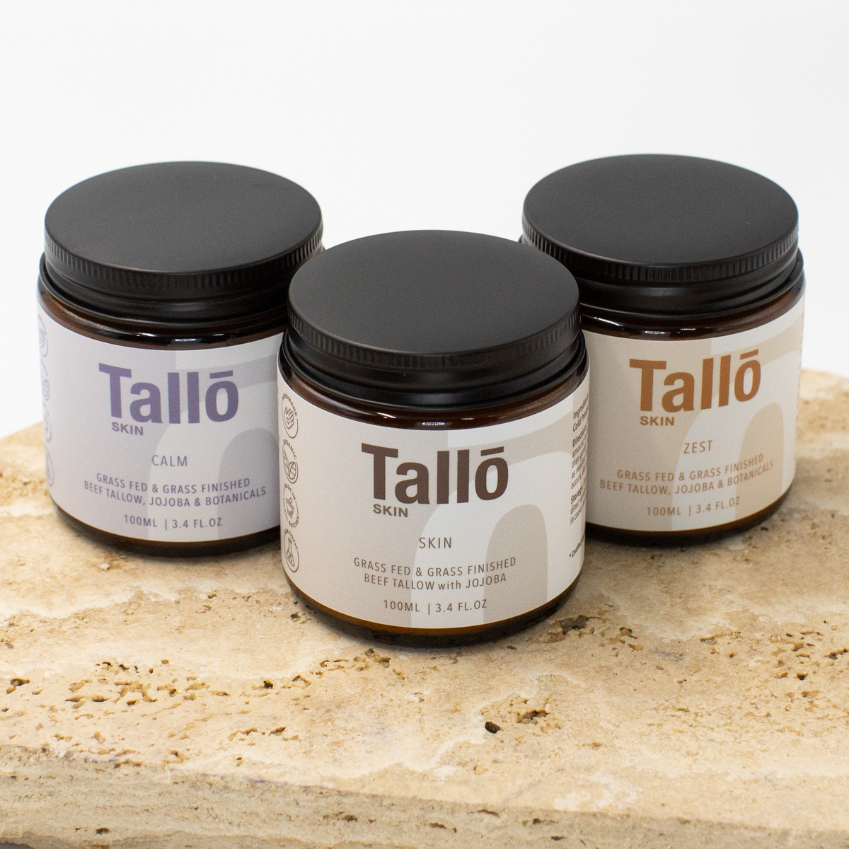 Three jars of Tallo skin care products on a stone surface