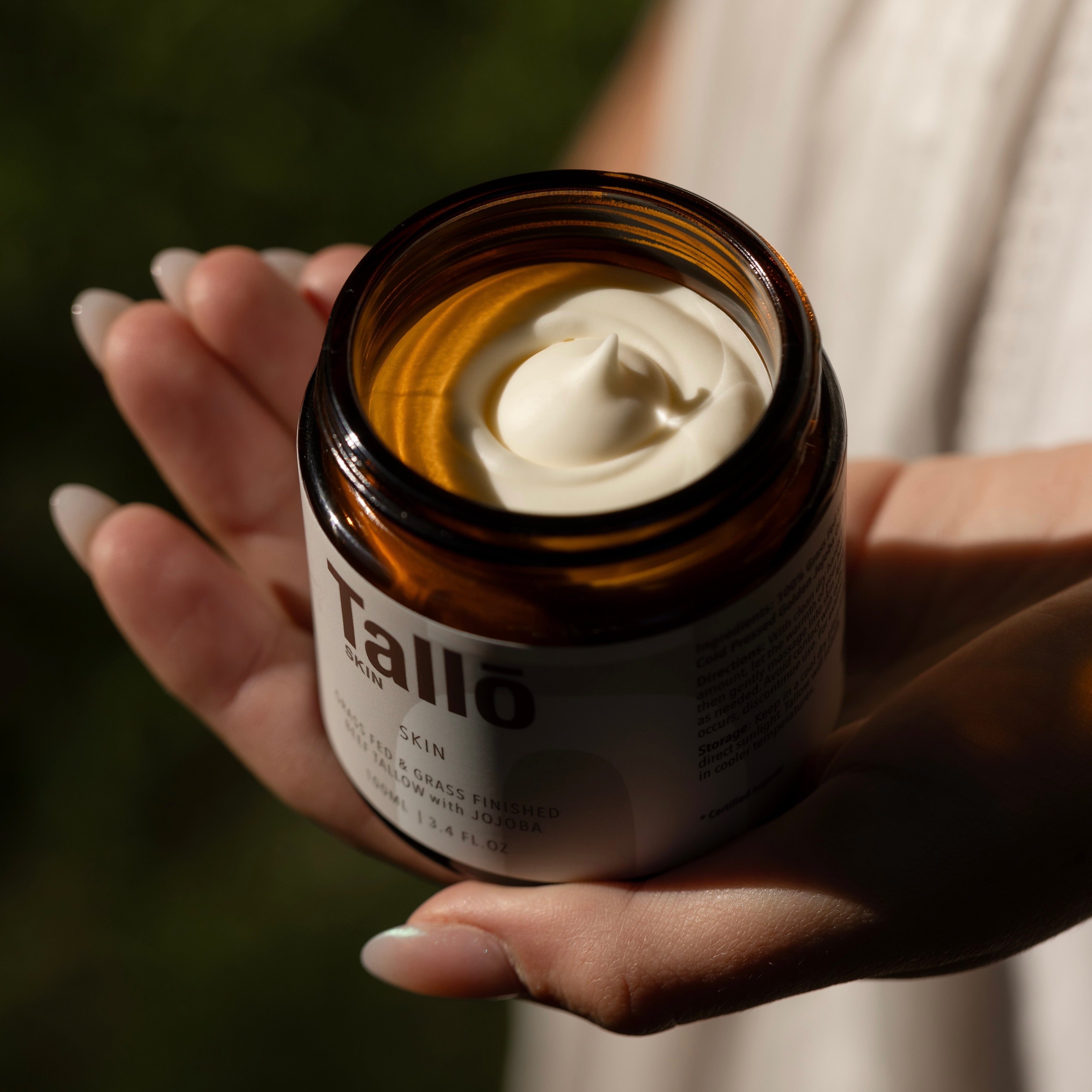 Hand holding a jar of Tallo skin tallow skincare product with visible cream.