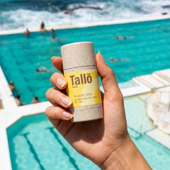 Hand holding a Tallo skin tallow sunscreen product with a bondi beach pool and people in the background